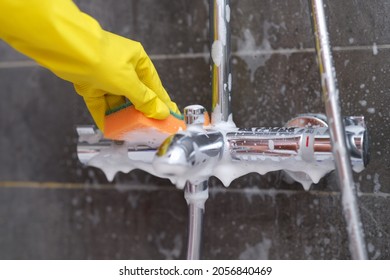 Hand In Yellow Glove Washes Chrome-plated Mixer With Washcloth In Bathroom