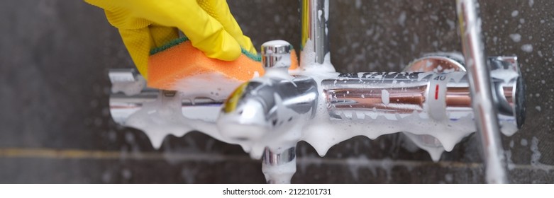 Hand In Yellow Glove Washes Chrome-plated Mixer With Washcloth In Bathroom