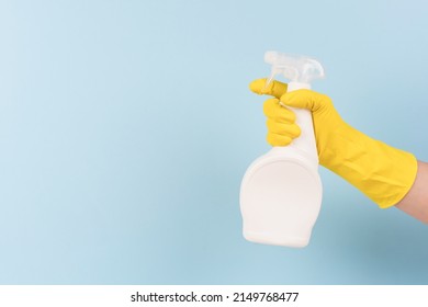 Hand in yellow protective rubber glove holding spray bottle with detergent against blue background with copy space. Cleaning product for different kitchen or bathroom surfaces. Bleach. Mockup