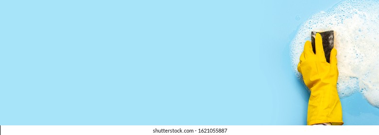 Hand in a yellow rubber glove holds a cleaning sponge and wipes a soapy foam on a blue background. Cleaning concept, cleaning service. Banner. Flat lay, top view - Powered by Shutterstock