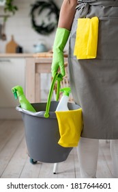 A hand in a yellow rubber glove holds a bucket of cleaning supplies. Professional house cleaning service, housekeeping. Concept of hygiene and cleanliness in the kitchen. Ready for work