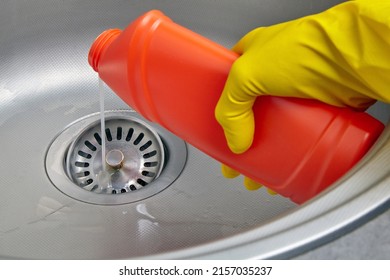 Hand in yellow rubber glove pour sewer pipe cleaner down the kitchen sink drain. Kitchen and drain cleaning work