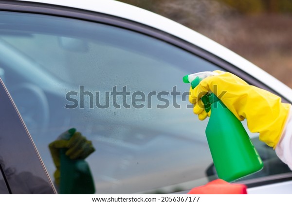 A hand in a yellow rubber glove sprays water\
from a spray bottle onto a car window on a warm autumn day. Wet\
cleaning. Selective focus.\
Close-up