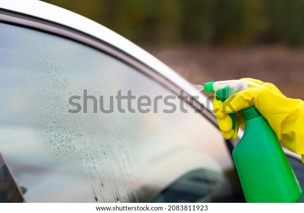 A hand in a yellow rubber glove sprays water
from a spray bottle onto a car window on a warm autumn day. Wet
cleaning. Selective focus.
Close-up