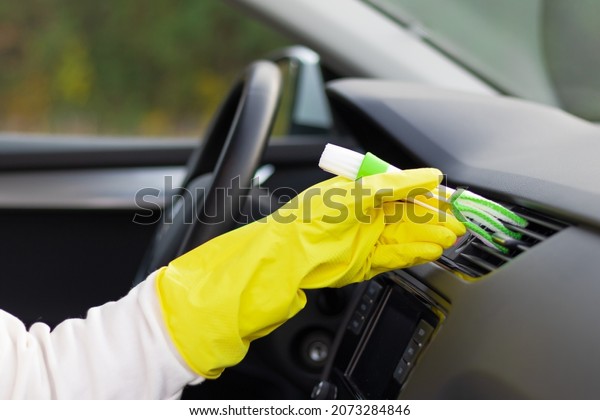 A hand in yellow rubber gloves wipes the\
dashboard of a car from dust with a special brush on a bright\
autumn day. Selective focus.\
Close-up