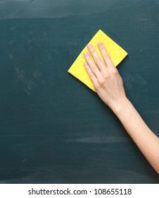 hand with a yellow sponge cleaning the chalkboard