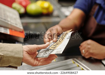 Hand of young African American female cashier passing discount coupon and receit to customer over checkout counter in supermarket