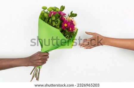 Hand of young african american guy gives bouquet of flowers to woman isolated on white studio background, close up. Surprise, love and relationship, birthday, anniversary, holiday celebration