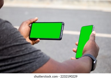 Hand of a young black African man
holding two green screen smartphones while sitting in the park - Powered by Shutterstock