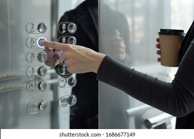 Hand of young businesswoman with drink pushing button inside elevator while going back to office on fifth floor at coffee break