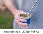 Hand of young caucasian man holding cup of mate, traditional infusion in many South American countries. Blurred background with copy space for text