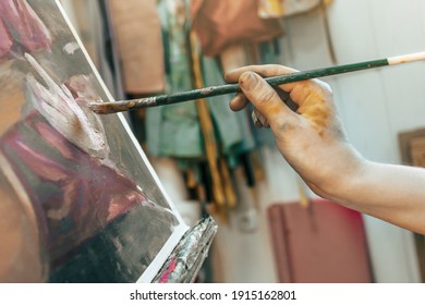 Hand of a young female artist close-up paints an oil painting during the day, using a brush for painting in a creative art studio, where the canvas is on an easel - Powered by Shutterstock