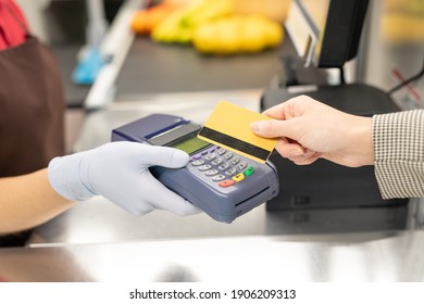 Hand of young female cashier in uniform and protective gloves holding payment terminal while one of consumers paying by credit card