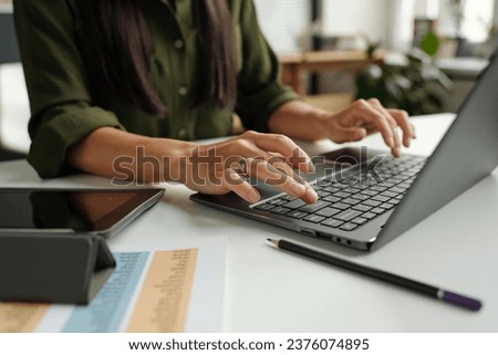 Hand of young female teacher or student typing on laptop keyboard while sitting by desk in front of camera and answering task questions