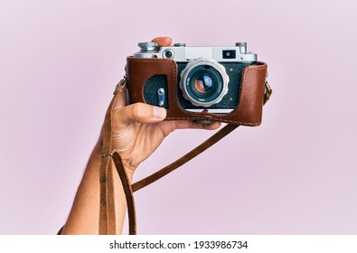 Hand Of Young Hispanic Man Holding Vintage Camera Over Isolated Pink Background.