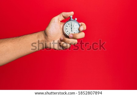 Hand of young hispanic man using stopwatch over isolated red background.