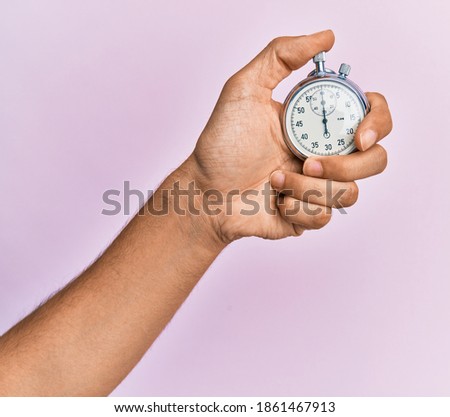 Hand of young hispanic man using stopwatch over isolated pink background.