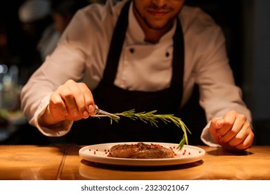Hand of young male chef putting aromatic herb on top of roasted meat