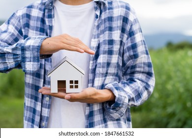 Hand Of Young Man Covering A House Model Metaphor Home Protection, Estate With Insurance, Mortage Or Loan Concept.