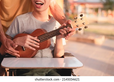 Hand Of Young Man With Disability Holding Ukulele And Singing, Playing With Music Therapy On The Outdoor Nature Background,Vacation Hobby Activity With Family Activity And Mental Health Concept.