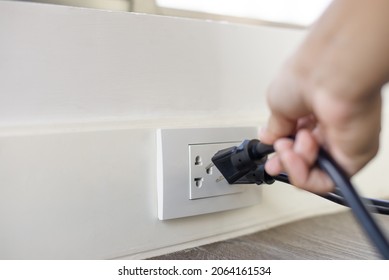 In The Hand Of A Young Man Holding A Power Cord To Unplug Unused Appliances To Save Energy, Save Money.