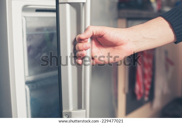 The hand of\
a young man is opening a freezer\
door