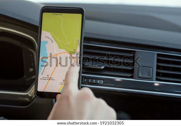 Hand of young man sitting in car and pointing at\
map on screen of smartphone while choosing place where he going to\
travel