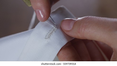 A Hand Of A Young Seamstress Sewing A White Cloth Tailoring According To The Tradition Of Tailors. The Dressmaker Uses Perfectly Needle And Thread To Sew