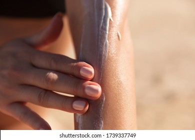 Hand of a young woman applying sun cream or sunscreen on her tanned arm to protect her skin from the sun. Shot on a sunny day with blurry sand in the background.  - Powered by Shutterstock