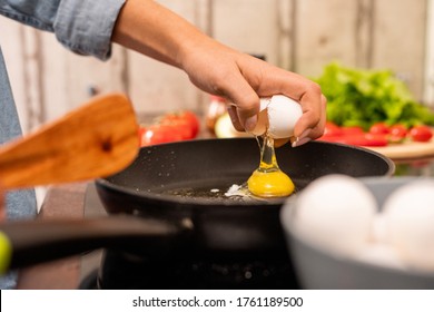 Hand Of Young Woman Breaking Fresh Egg On Frying Pan Standing On Electric Stove While Cooking Breakfast In The Morning