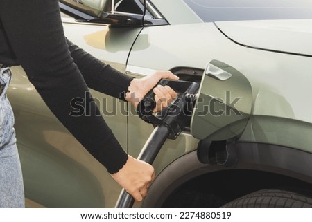 Hand of a young woman driving an EV or electric car holding DC power plug to her vehicle's green electric vehicle battery socket : Clean energy vehicle alternative energy is becoming popular concept. Foto stock © 