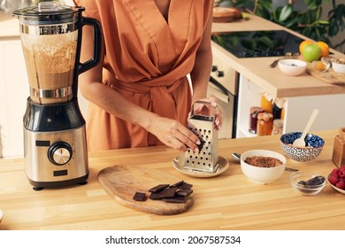 Hand Of Young Woman Grating Dark Chocolate For Tasty Homemade Cocoa Dessert Or Smoothie In Electric Blender