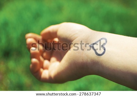 Hand of young woman with heart tattooed in it, on green nature background