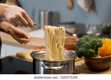 Hand Of Young Woman Holding Hot Boiled Spaghetti On Spoon Over Metallic Pan With Water On Electric Stove While Cooking Pasta