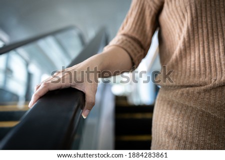 Hand of young woman touching the escalator during Coronavirus pandemic,risk of contagious or contamination of COVID-19,virus,bacteria or germs avoid touching handrail of escalator in public places