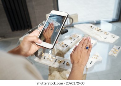 Hand of young woman trying on ring with blue gemstone and taking photograph over display with jewelry - Powered by Shutterstock