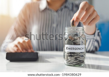 Hand of Young women putting Coins in a glass jar on the table. Saving for emergency concept.