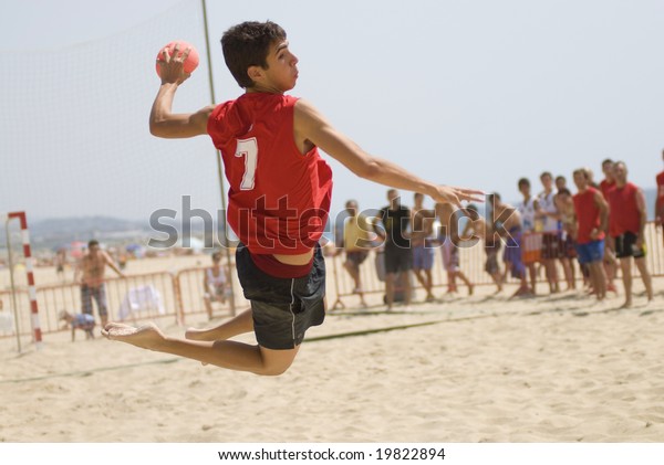 Handball player jumping with the ball trying\
to score a goal on a handball beach\
match
