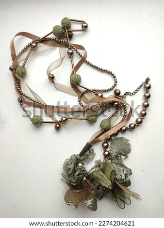 Handcrafted layered jewelery necklace with copper beads, green lace and brown ribbon on a white table. Selected focus 