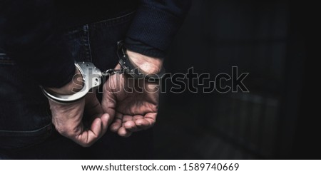 handcuffed arrested man behind prison bars. copy space