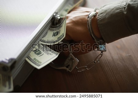 Handcuffed Hand Reaching For Dollar Bills in Briefcase Depicting Financial Crime and Corruption