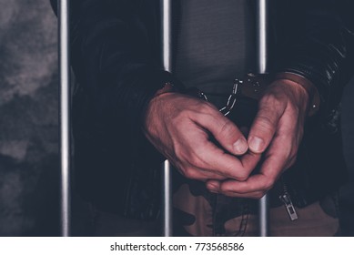 Handcuffed man behind prison bars. Arrested criminal male person imprisoned.