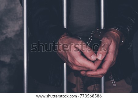 Handcuffed man behind prison bars. Arrested criminal male person imprisoned.