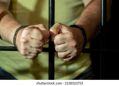 A Handcuffed Man Clenches His Fists Behind Bars In A Cell. Concept: A Prisoner In A Courtroom, A Court Sentence To A Convicted Person, A Prison Term 1.