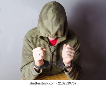 The handcuffed offender regrets the crime and hides his face. The arrested man in handcuffs. - Shutterstock ID 2102539759