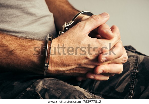 Handcuffed soldier in military army clothes.\
Prisoner of war or arrested terrorist, close up of hands in\
handcuffs, selective\
focus.