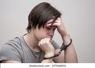 A Handcuffed Teenager Sits On A Grey Background. Juvenile Delinquent, Criminal Liability Of Minors. Members Of Youth Criminal Groups And Gangs.