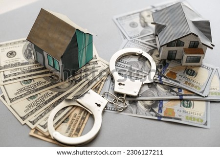 handcuffs, dollars, house figure on wooden background. violation of law. real estate fraud.