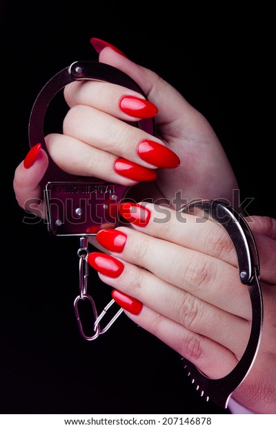 Handcuffs in hand with red painted nails\
studio shot at black\
background.