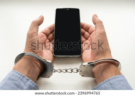 Handcuffs man's hands and mobile phone. Concept of addiction. a phone fraudster in handcuffs with a smartphone.